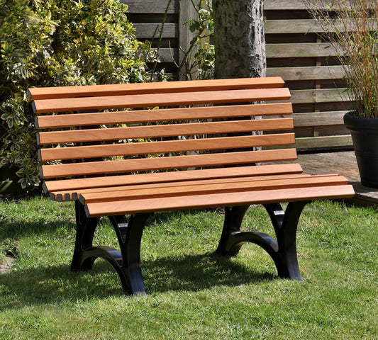 Bank "Amrum" in Holzoptik vor einem Busch und einer Holzpalisade in Gartenlandschaft