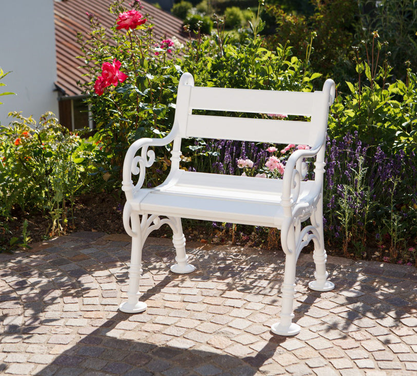Weißer Stuhl "Linderhof" vor Blumenbeet in Gartenlandschaft, im Hintergrund unscharf erkennbare Häuser