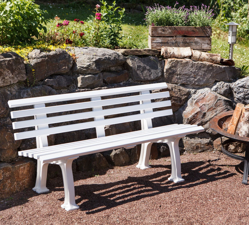 Weiße Bank "Sylt" in einer Gartenlandschaft, positioniert vor einer Natursteinmauer, mit einer Feuerschale daneben