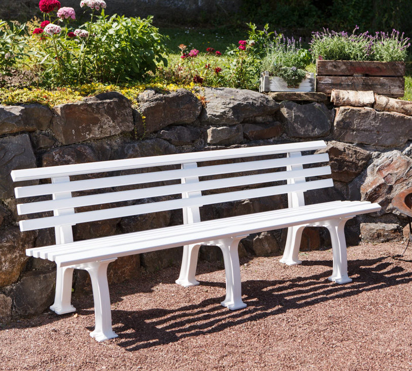 Weiße Bank "Juist" in einer Gartenlandschaft, positioniert vor einer Natursteinmauer, mit einer Feuerschale daneben