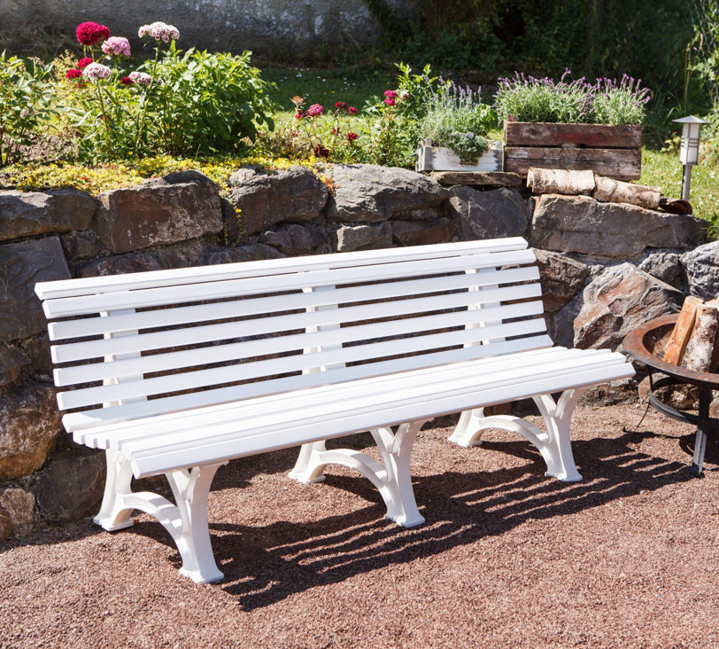 Weiße Bank "Borkum" in einer Gartenlandschaft, positioniert vor einer Natursteinmauer, mit einer Feuerschale daneben