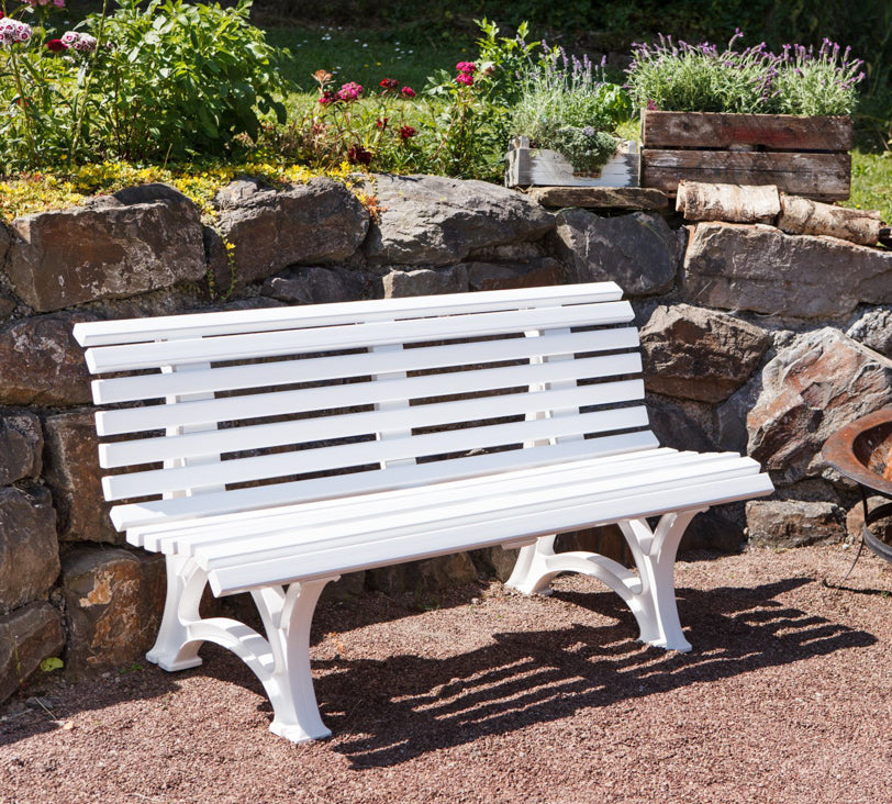 Weiße Bank "Helgoland" in einer Gartenlandschaft, positioniert vor einer Natursteinmauer, mit einer Feuerschale daneben