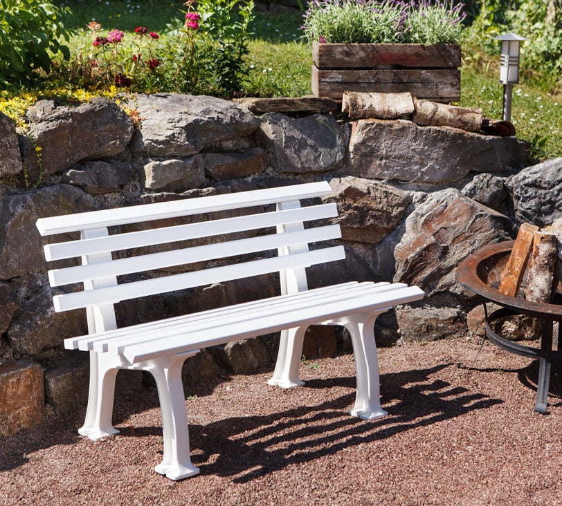 Weiße Bank "Ibiza" in einer Gartenlandschaft, positioniert vor einer Natursteinmauer, mit einer Feuerschale daneben