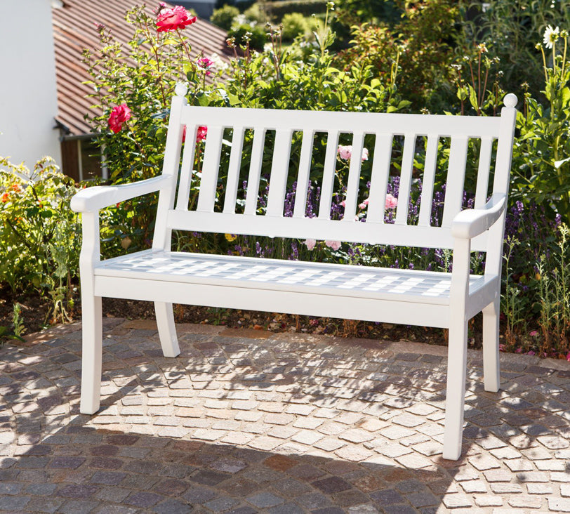 Weiße Bank "Hohenzollern" Zweisitzer vor Blumenbeet in Gartenlandschaft, im Hintergrund unscharf erkennbare Häuser