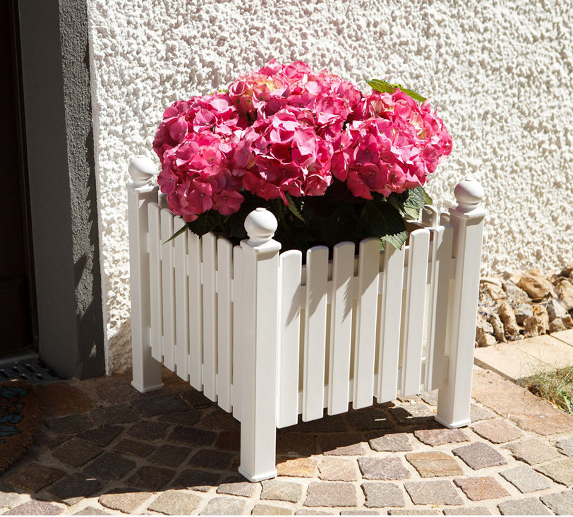 Pflanzkasten Landhaus in Weiß vor einer Hauswand auf einem Steinboden mit einer Blume darin